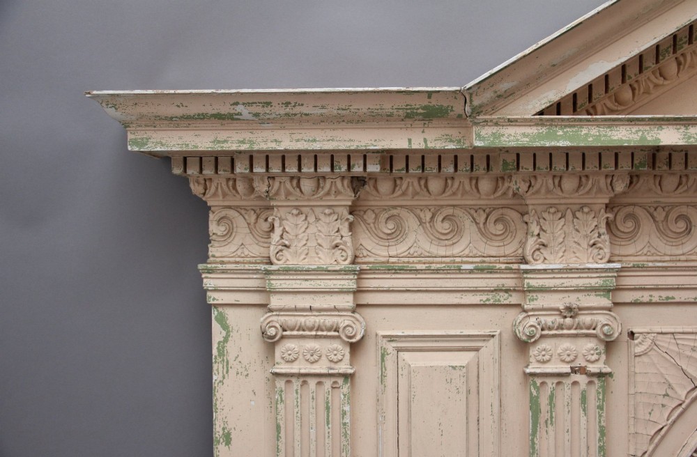 An 18th-century carved pine architectural overmantel featuring a broken pediment, fluted pilasters, dentil mouldings, and a central circular aperture in distressed off-white paint. View X