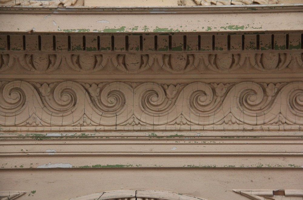 An 18th-century carved pine architectural overmantel featuring a broken pediment, fluted pilasters, dentil mouldings, and a central circular aperture in distressed off-white paint. View XV