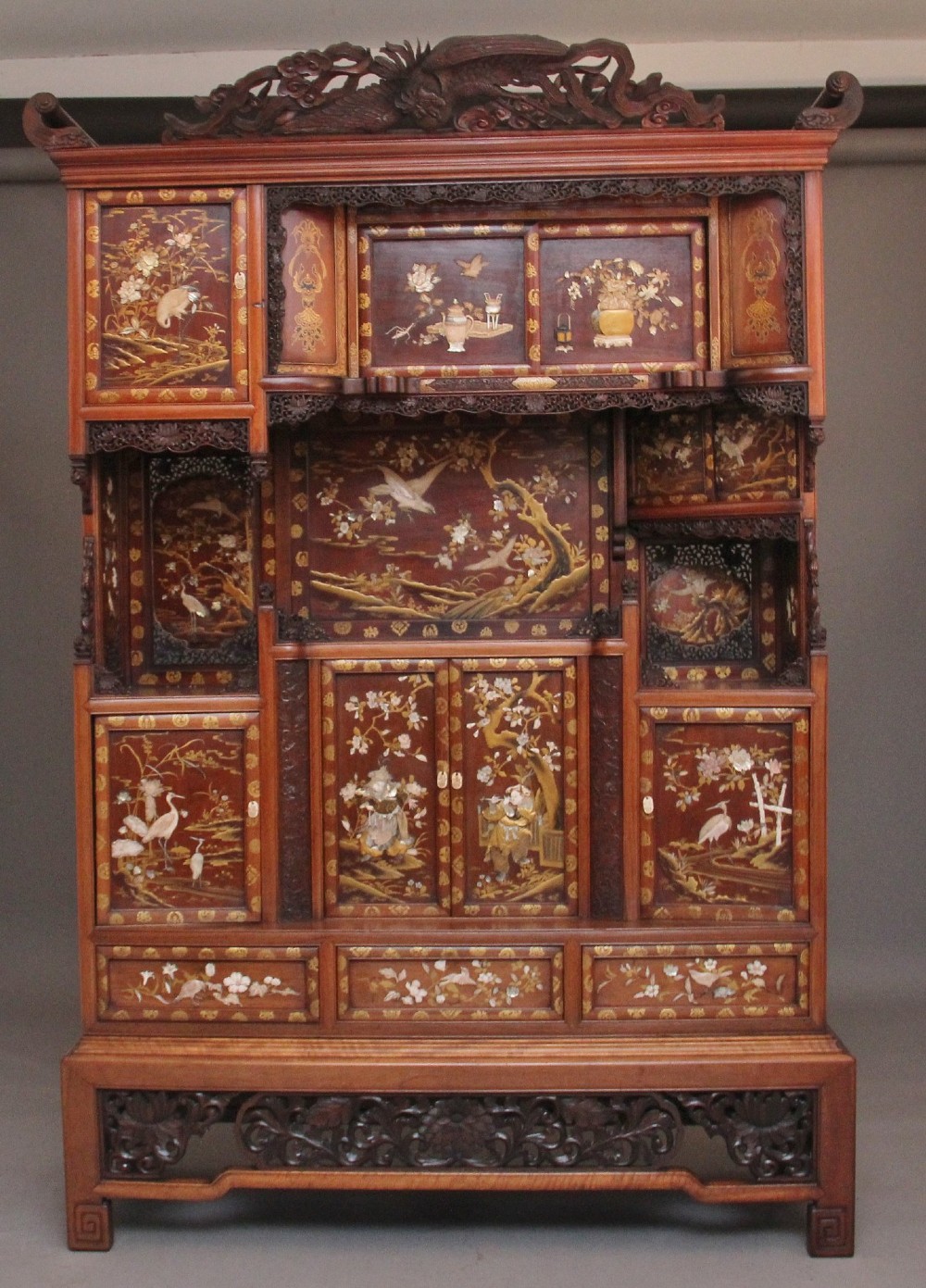 A large 19th-century Japanese hardwood Shodona cabinet featuring asymmetric shelves, carved dragon cresting, and panel doors adorned with lacquer and mother-of-pearl bird motifs.