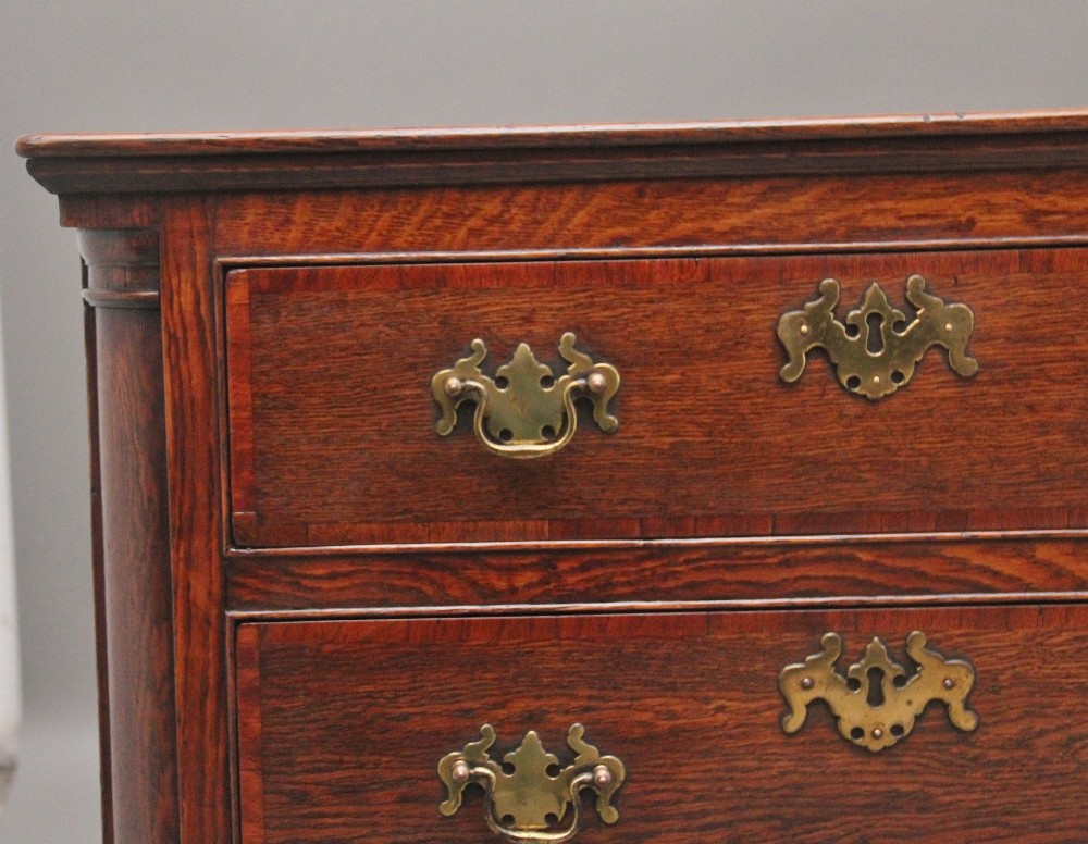 A large 18th-century oak dresser base featuring brass swan-neck handles, multiple drawers, a central panelled cupboard, and bracket feet. View IV