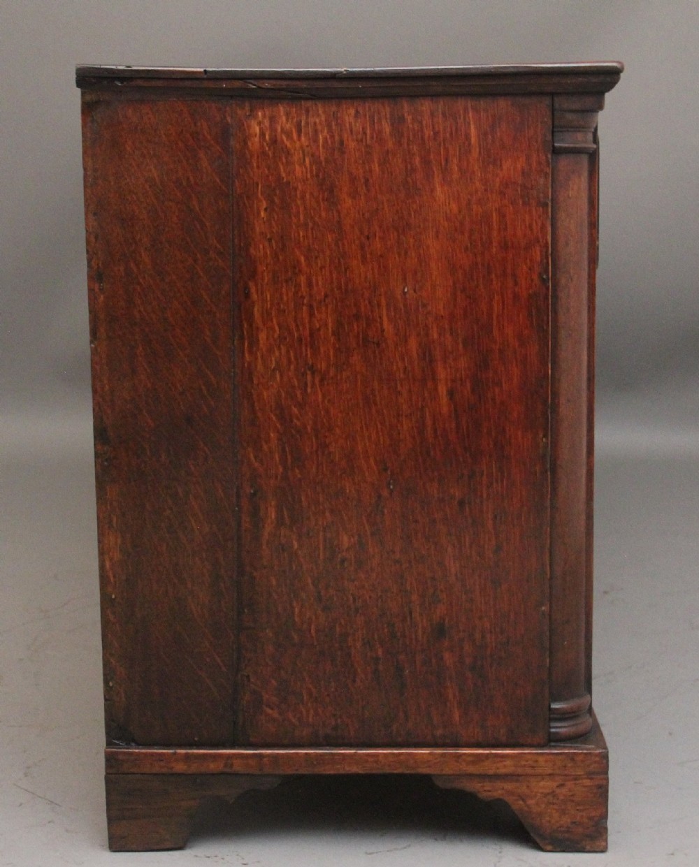 A large 18th-century oak dresser base featuring brass swan-neck handles, multiple drawers, a central panelled cupboard, and bracket feet. View VII