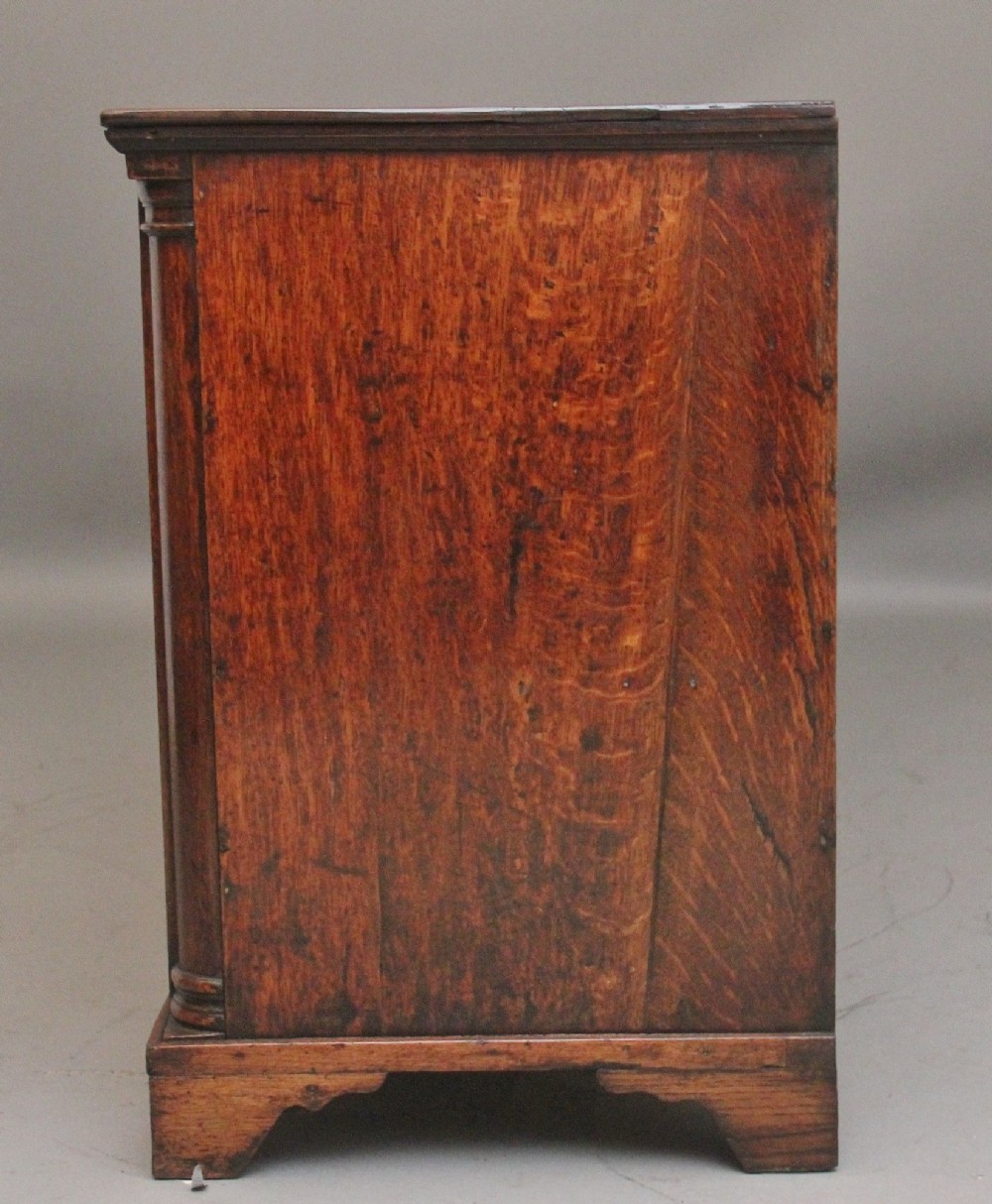 A large 18th-century oak dresser base featuring brass swan-neck handles, multiple drawers, a central panelled cupboard, and bracket feet. View IX