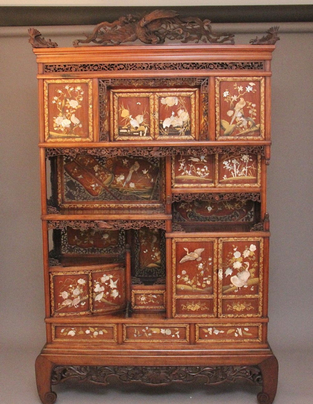A 19th-century Japanese Meiji period shodona display cabinet with asymmetrical lacquered doors, bird and floral shibayama inlays, and carved cresting.