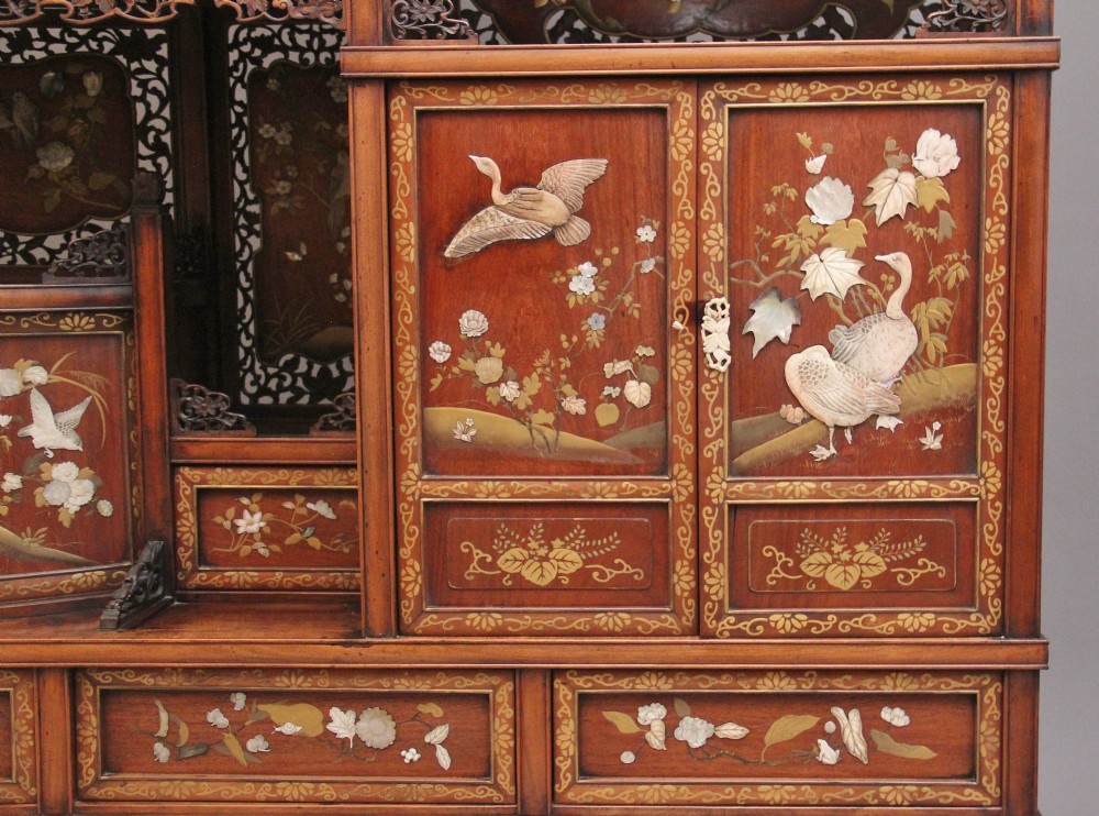 A 19th-century Japanese Meiji period shodona display cabinet with asymmetrical lacquered doors, bird and floral shibayama inlays, and carved cresting. View X