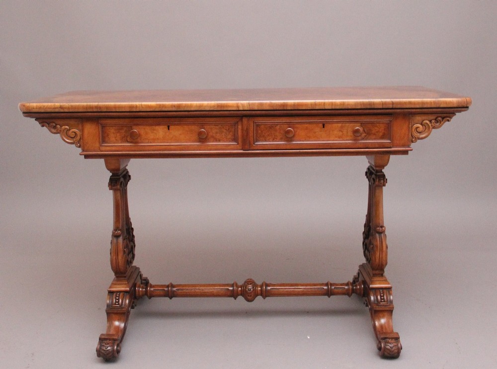A 19th-century burr walnut library table with two frieze drawers, carved scroll brackets, dual pedestal legs, and a central turned stretcher.