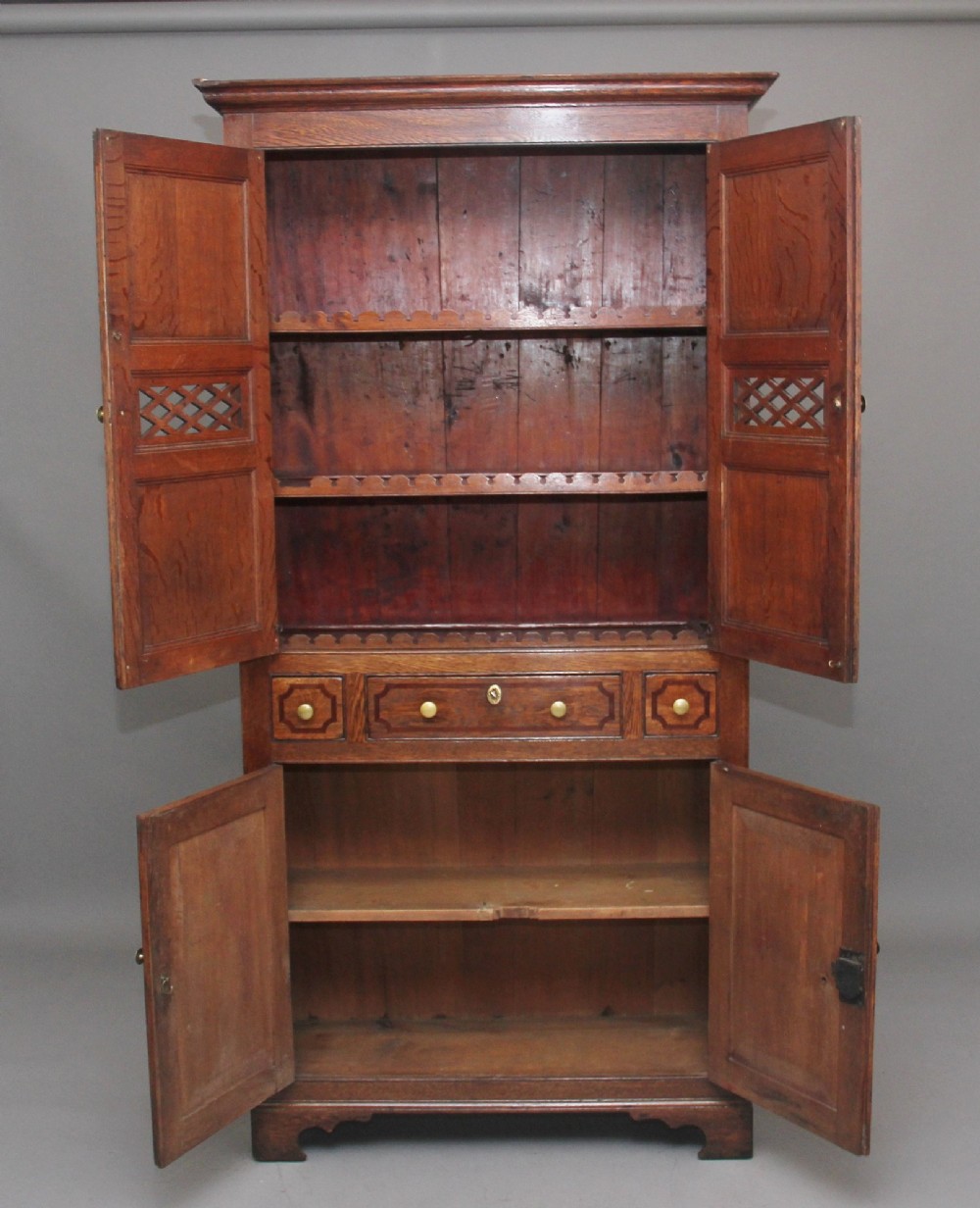 An early 19th-century dark oak food cupboard featuring pierced lattice ventilation panels, brass drawer handles, and panelled double doors. View II