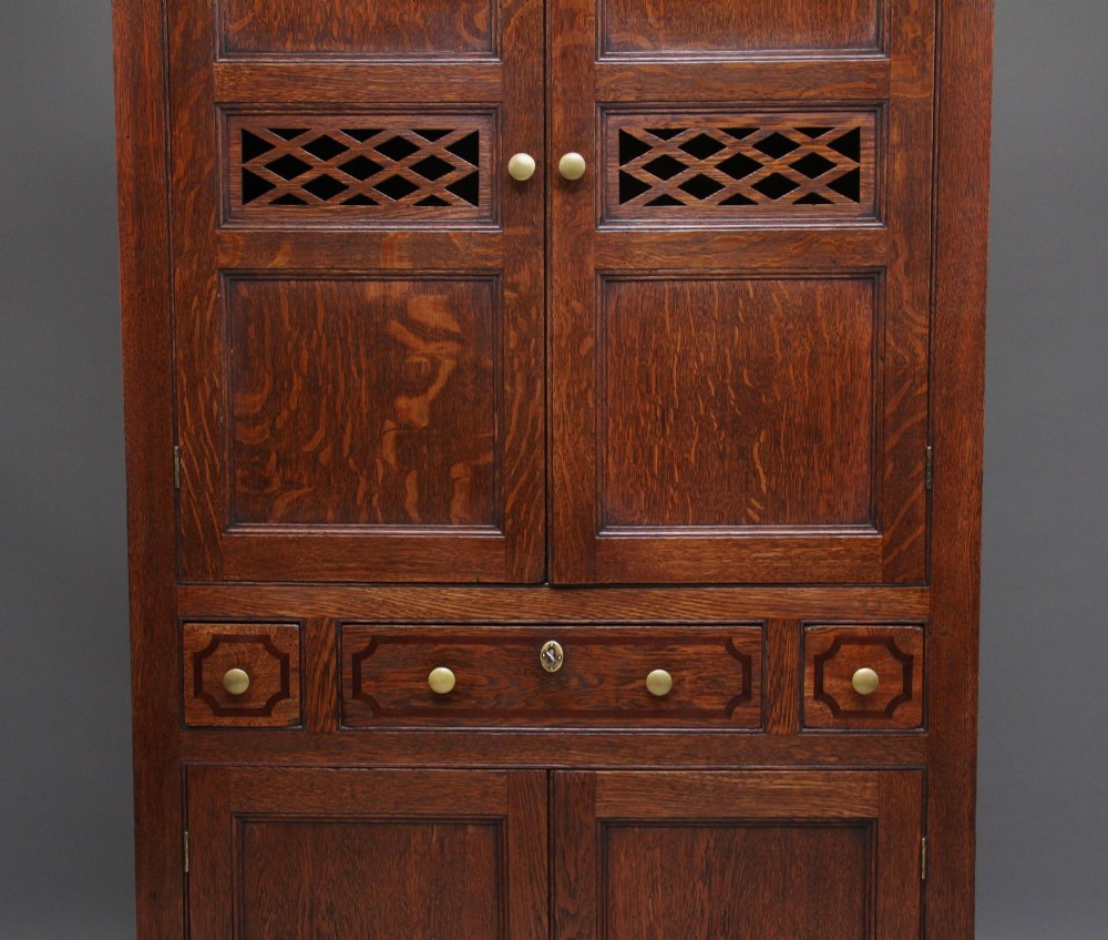 An early 19th-century dark oak food cupboard featuring pierced lattice ventilation panels, brass drawer handles, and panelled double doors. View VIII