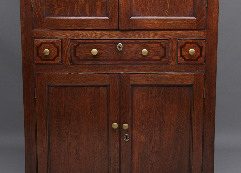 An early 19th-century dark oak food cupboard featuring pierced lattice ventilation panels, brass drawer handles, and panelled double doors. View IX