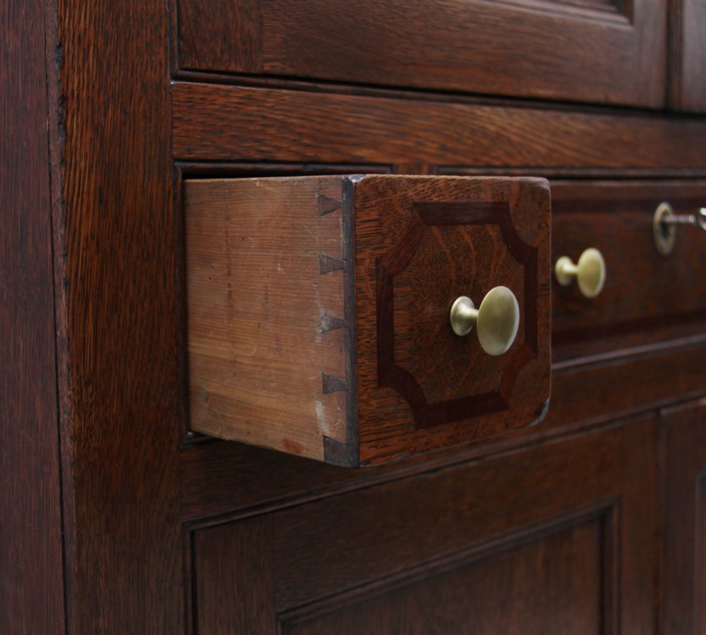 An early 19th-century dark oak food cupboard featuring pierced lattice ventilation panels, brass drawer handles, and panelled double doors. View XI