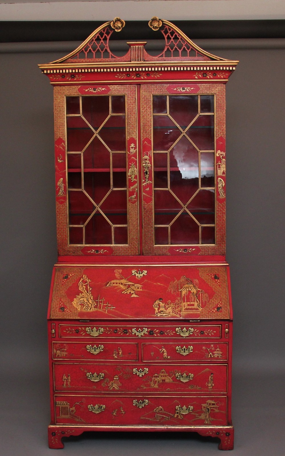 An early twentieth-century red lacquered Chinoiserie bureau bookcase decorated with gilded landscapes, double glazed doors, and brass drop handles.
