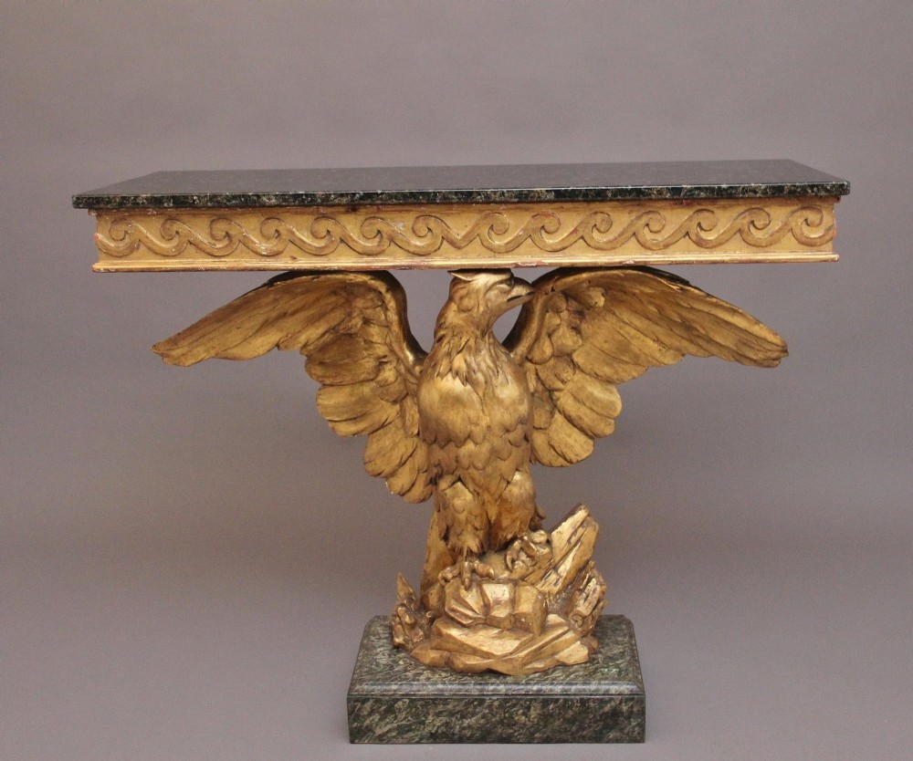 An early 20th-century console table featuring a dark marble top supported by a carved golden eagle pedestal on a matching marble base.