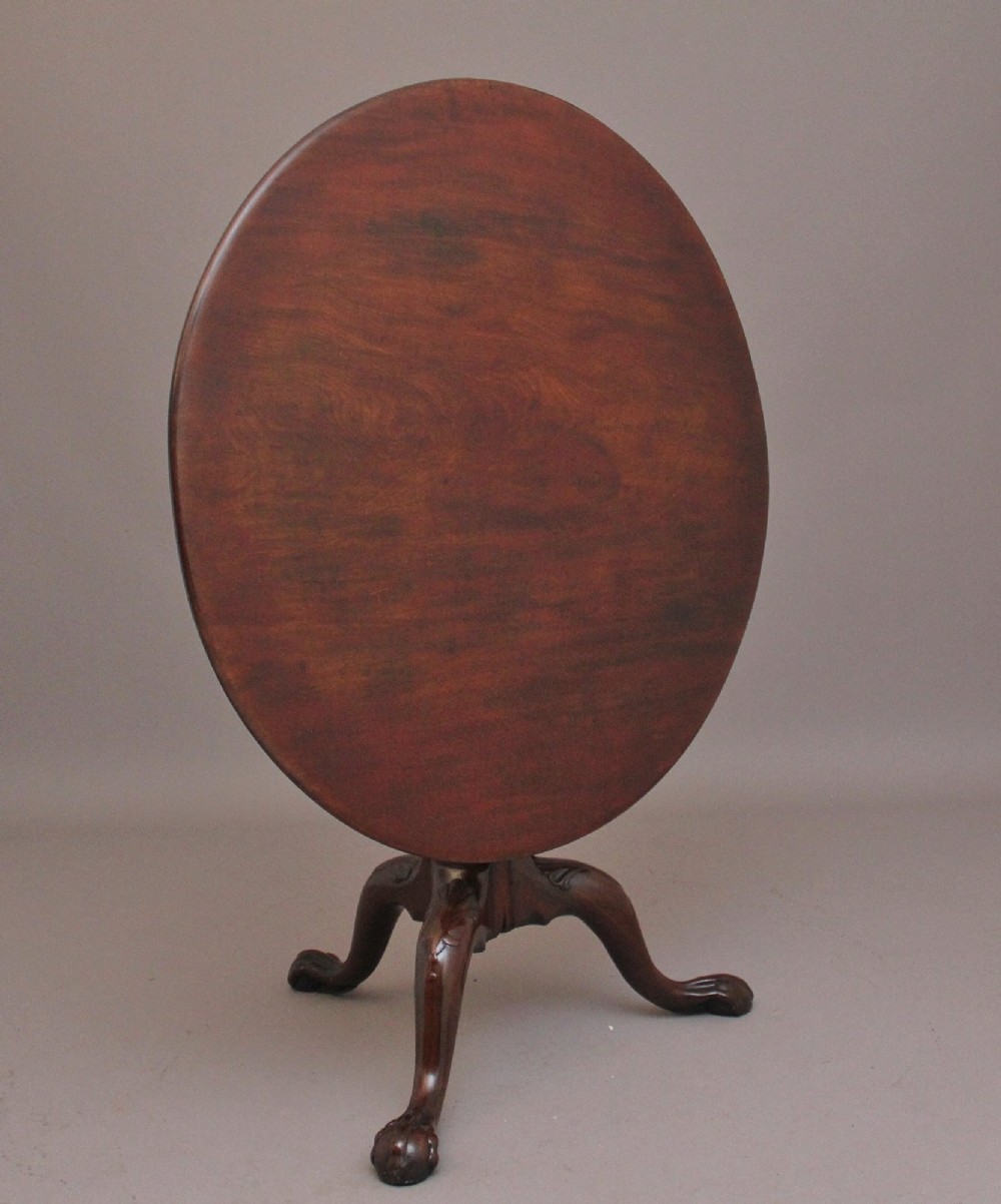 An 18th-century mahogany tripod table with its round top tilted upright on a turned column with three carved legs.