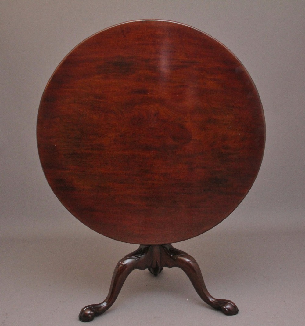 An 18th-century mahogany tripod table with its round top tilted upright on a turned column with three carved legs. View II