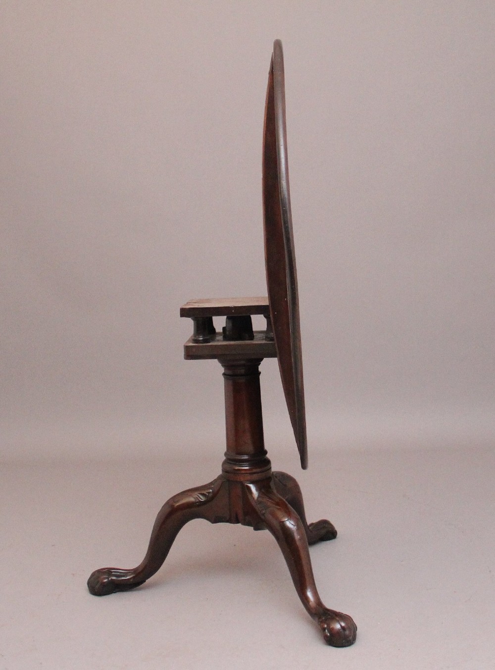 An 18th-century mahogany tripod table with its round top tilted upright on a turned column with three carved legs. View IV