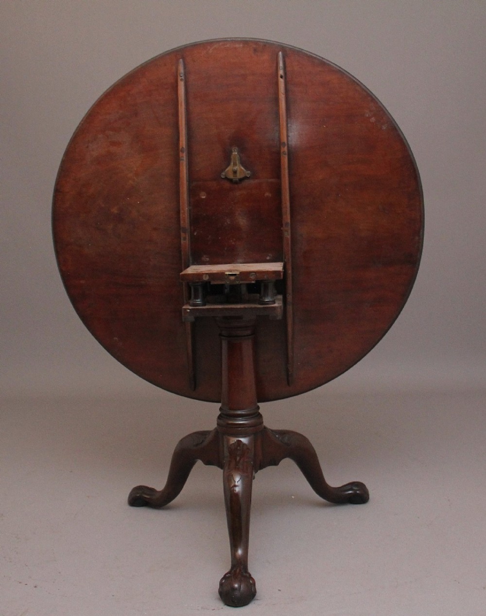 An 18th-century mahogany tripod table with its round top tilted upright on a turned column with three carved legs. View V