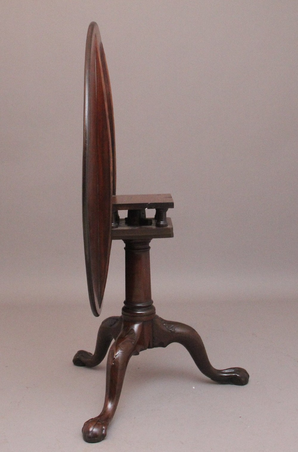 An 18th-century mahogany tripod table with its round top tilted upright on a turned column with three carved legs. View VI