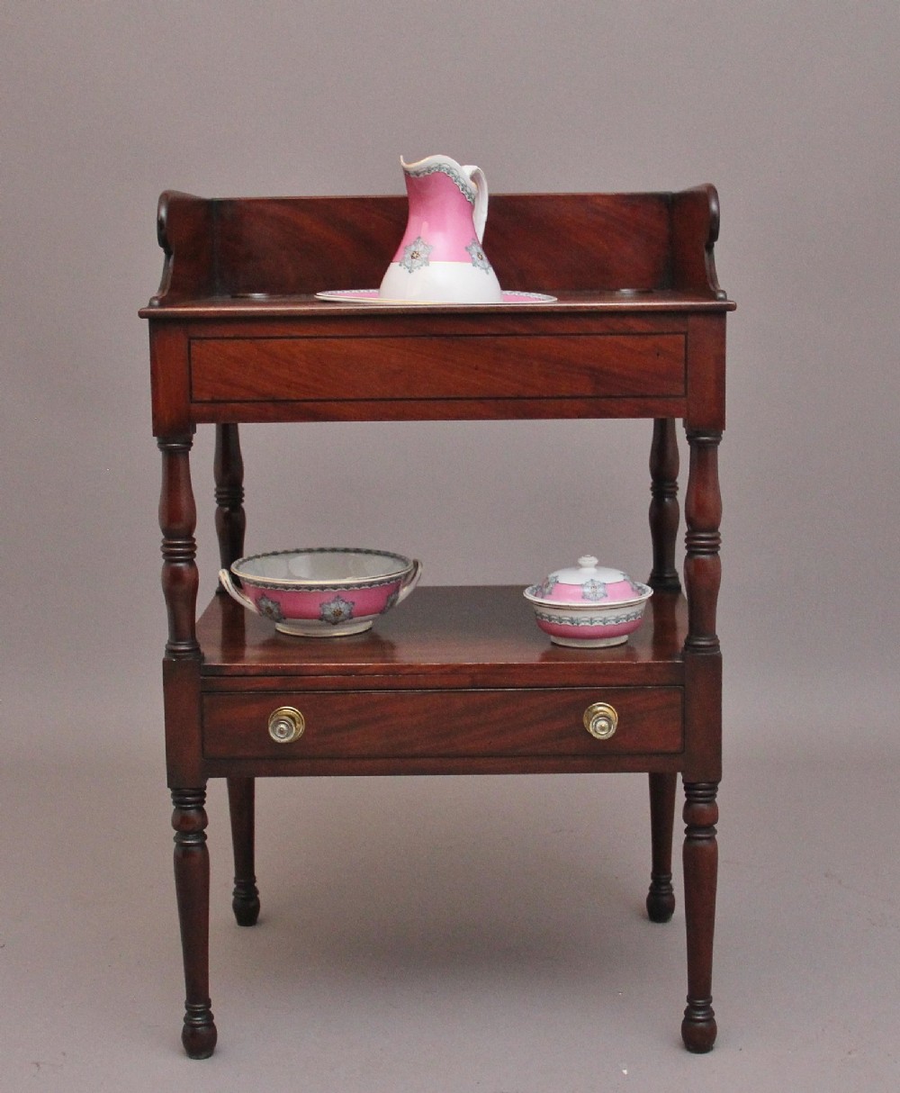 An early Victorian mahogany washstand featuring a gallery splashback top with circular aperture cutouts, a central open shelf, turned legs, and a bottom drawer with brass handles. View II