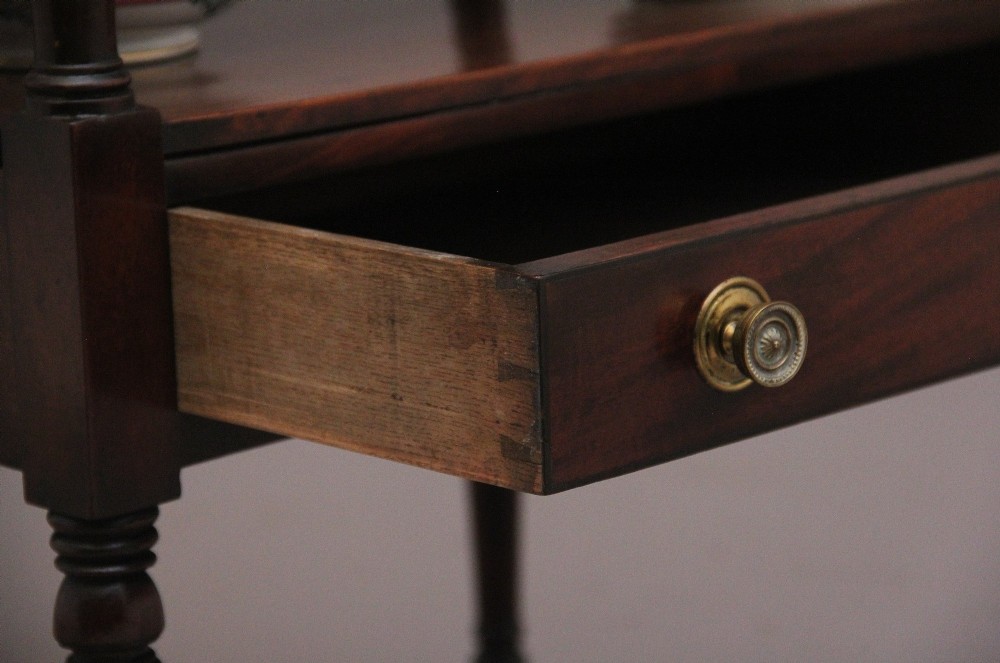 An early Victorian mahogany washstand featuring a gallery splashback top with circular aperture cutouts, a central open shelf, turned legs, and a bottom drawer with brass handles. View III