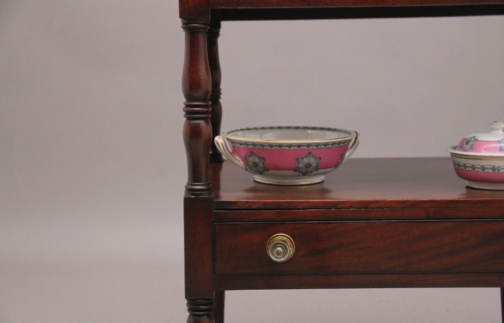 An early Victorian mahogany washstand featuring a gallery splashback top with circular aperture cutouts, a central open shelf, turned legs, and a bottom drawer with brass handles. View VIII