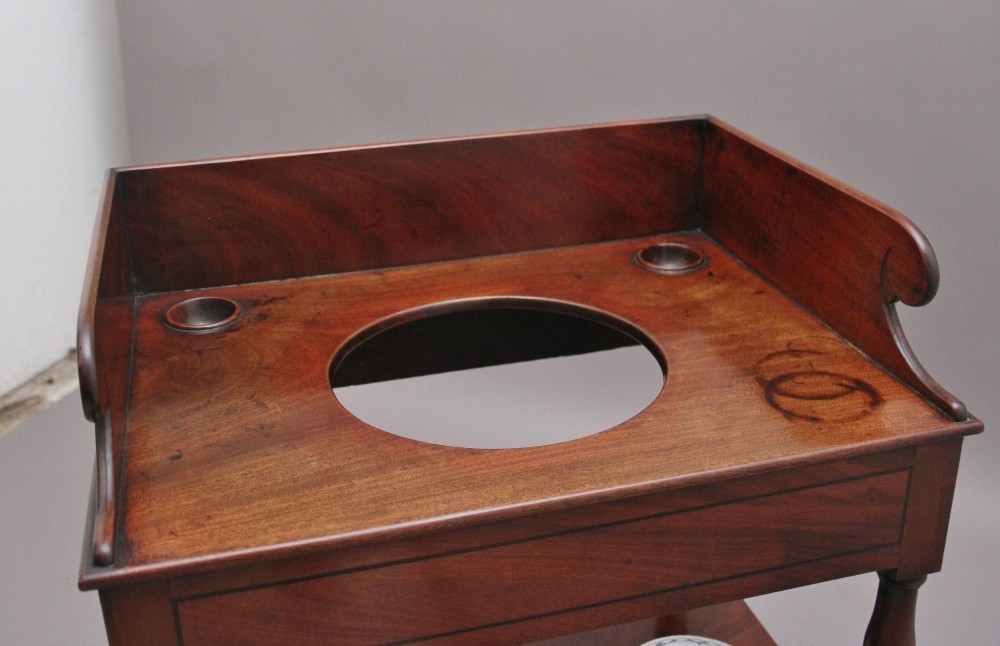 An early Victorian mahogany washstand featuring a gallery splashback top with circular aperture cutouts, a central open shelf, turned legs, and a bottom drawer with brass handles. View XI