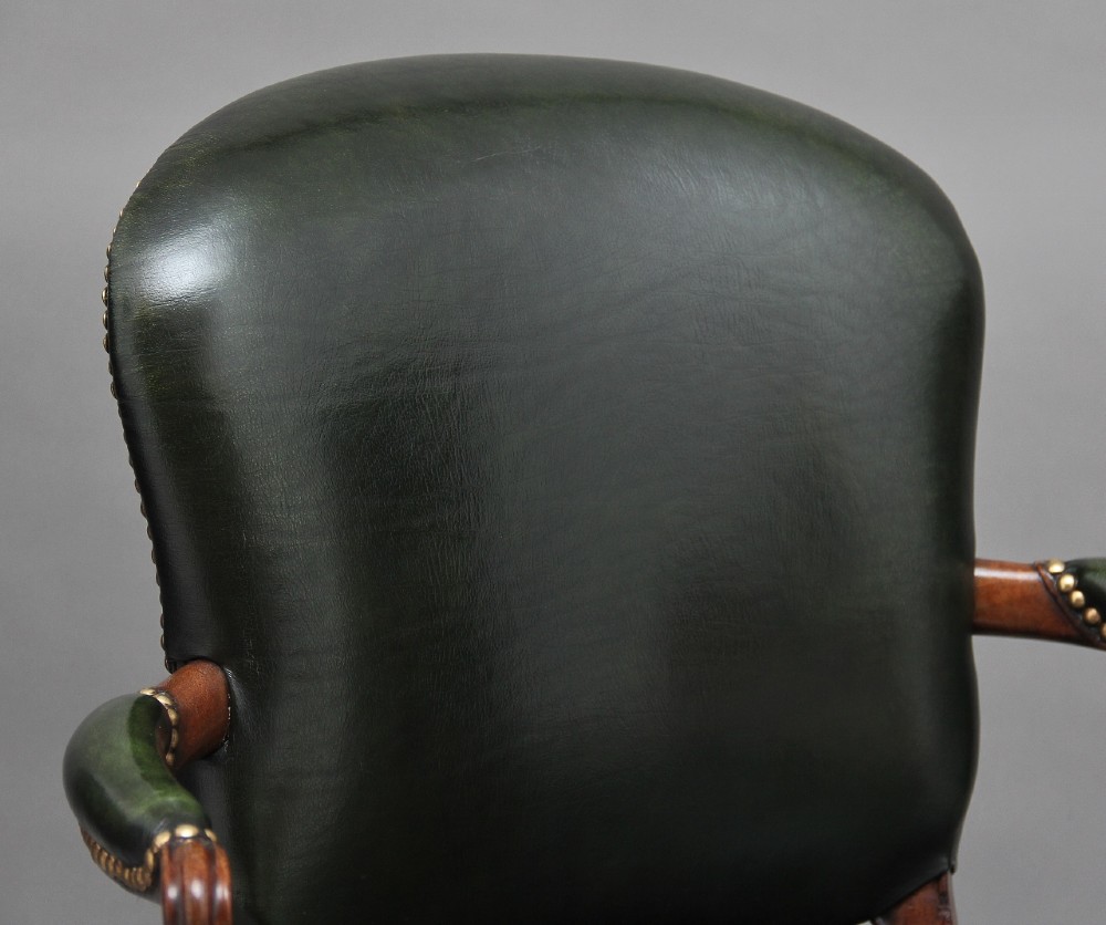 A 19th-century mahogany open armchair upholstered in dark green leather with brass studding and fluted front legs. View X
