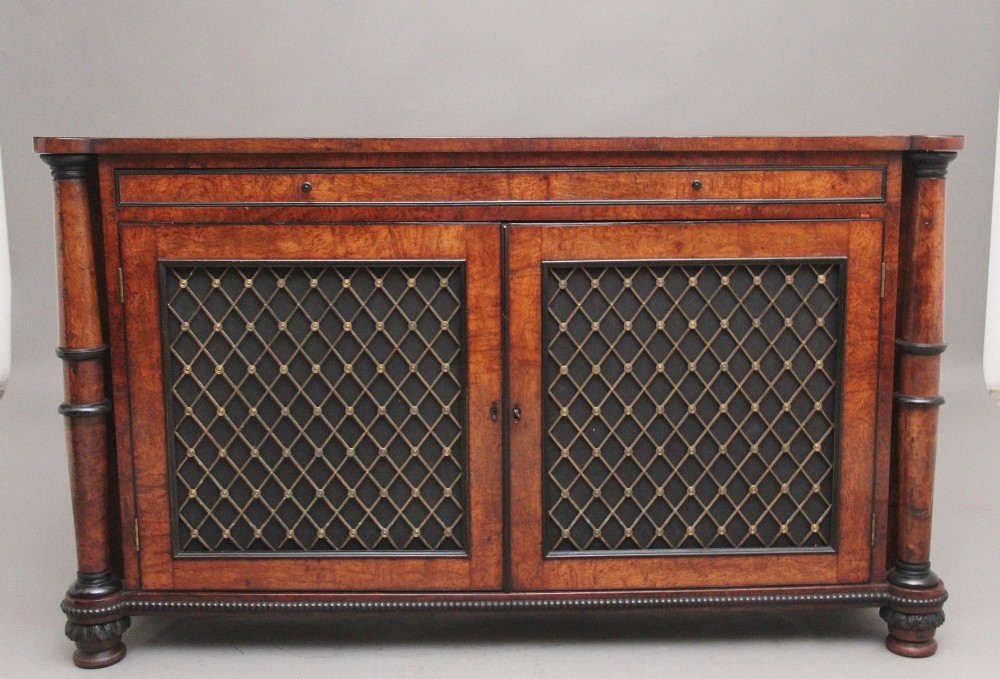 An early 19th-century Regency pollard oak side cabinet featuring two brass lattice grille doors, ebony stringing, and turned flanking columns.