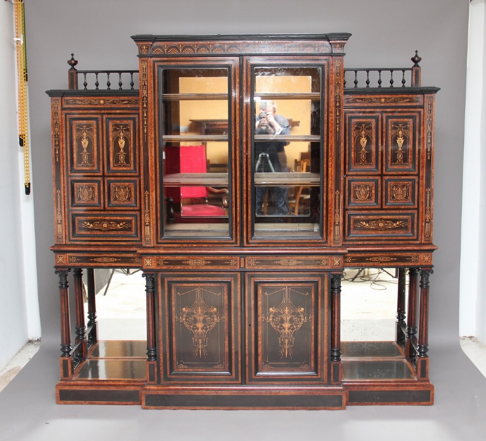 A large Victorian ebonised and walnut display cabinet with marquetry inlays, central glazed doors, and turned columns.