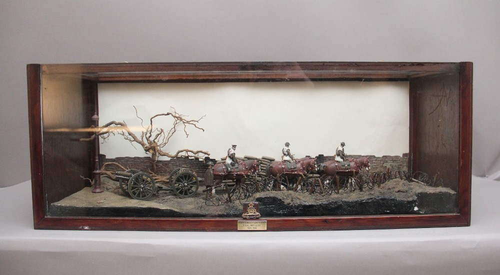 A glazed wooden display case containing an early 20th-century military diorama of a horse-drawn artillery team on a WWI battlefield scene.