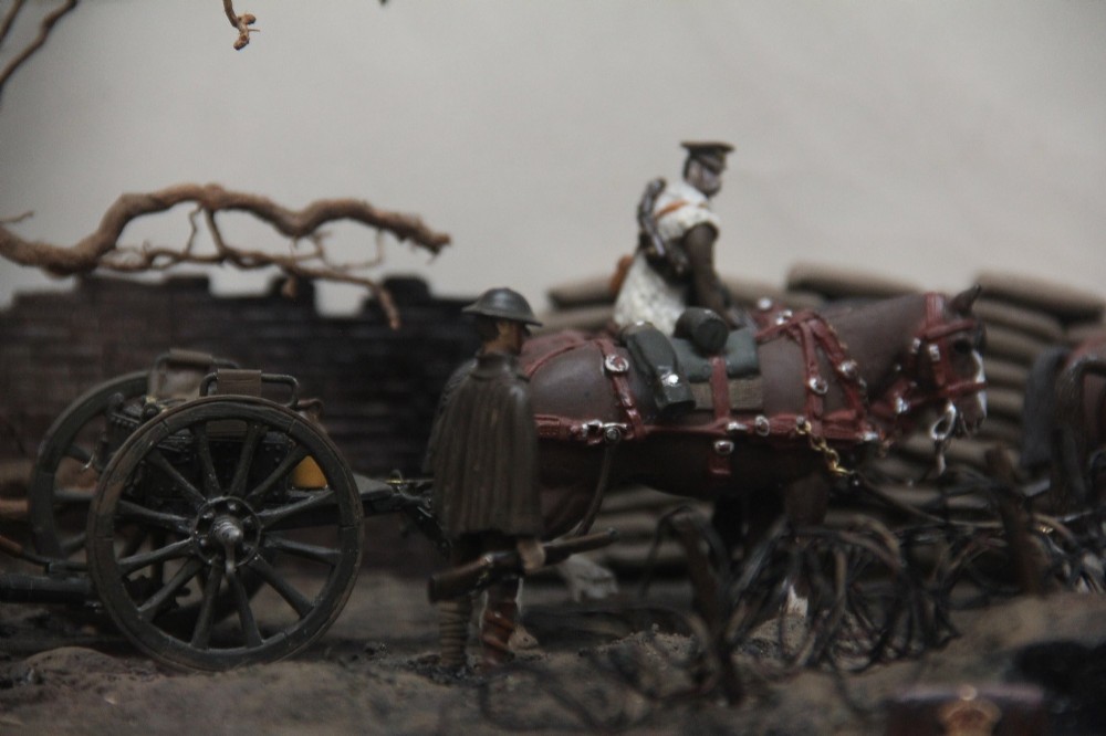 A glazed wooden display case containing an early 20th-century military diorama of a horse-drawn artillery team on a WWI battlefield scene. View VI