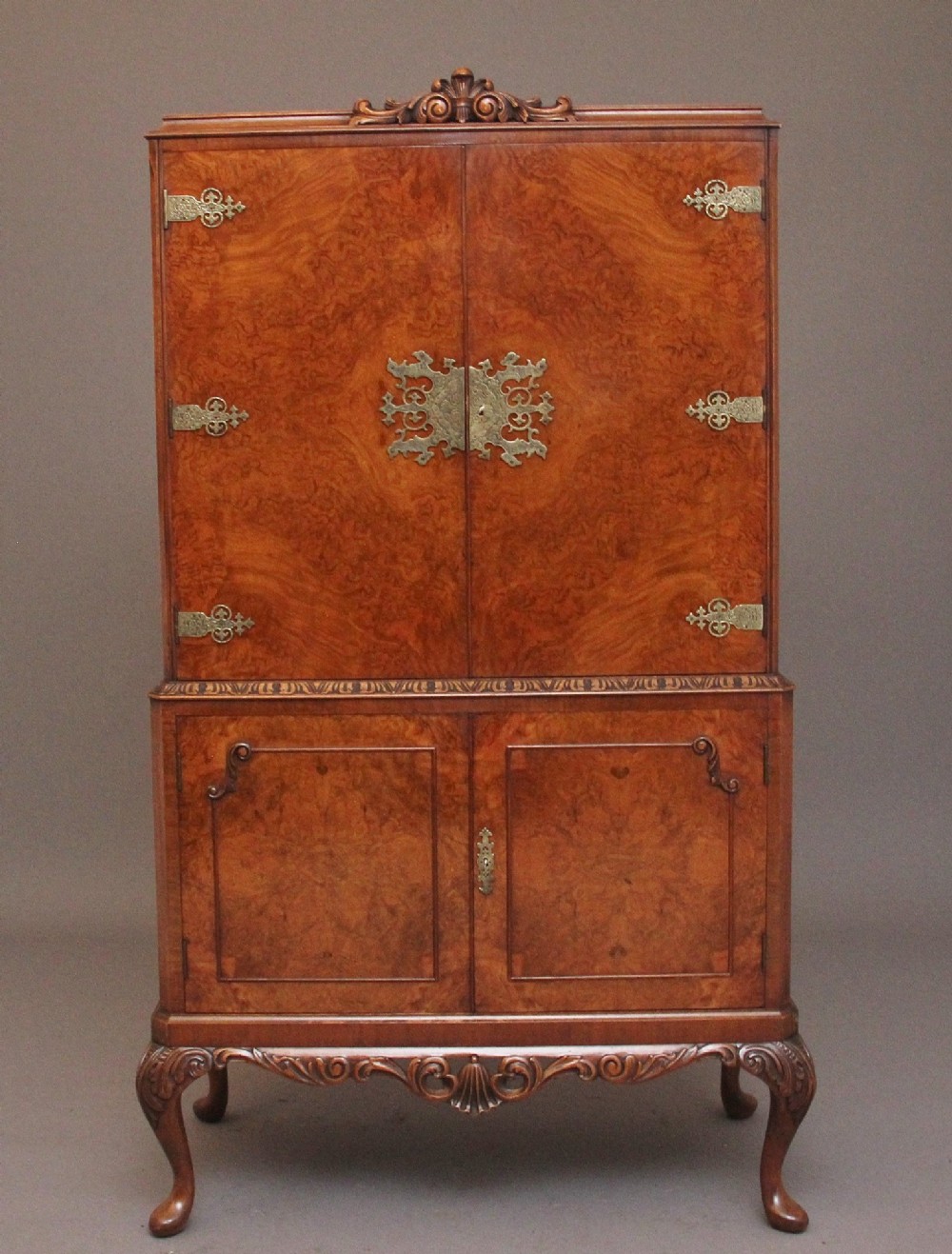 An early 20th-century burr walnut drinks cabinet with decorative pierced brass strap hinges, double doors, and carved cabriole legs.