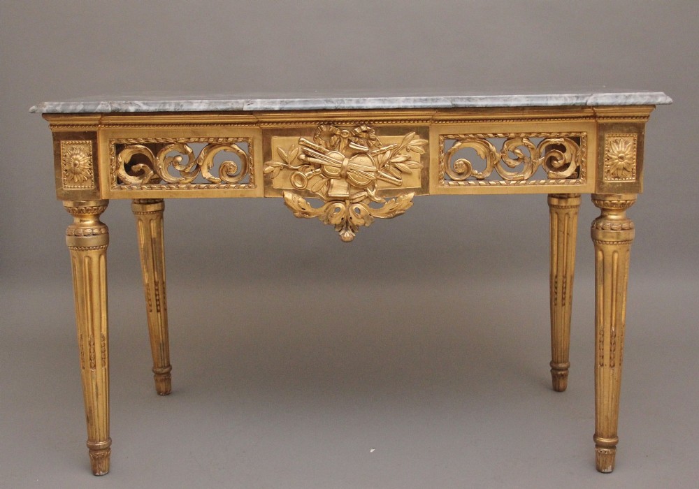 An 18th-century Italian Neoclassical console table featuring a grey marble top, pierced carved giltwood apron with central trophy carving, and fluted tapered legs.
