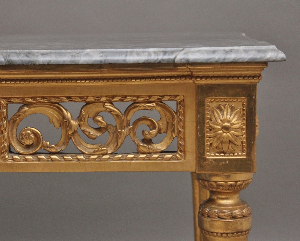 An 18th-century Italian Neoclassical console table featuring a grey marble top, pierced carved giltwood apron with central trophy carving, and fluted tapered legs. View IV