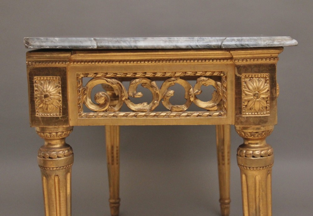 An 18th-century Italian Neoclassical console table featuring a grey marble top, pierced carved giltwood apron with central trophy carving, and fluted tapered legs. View VI