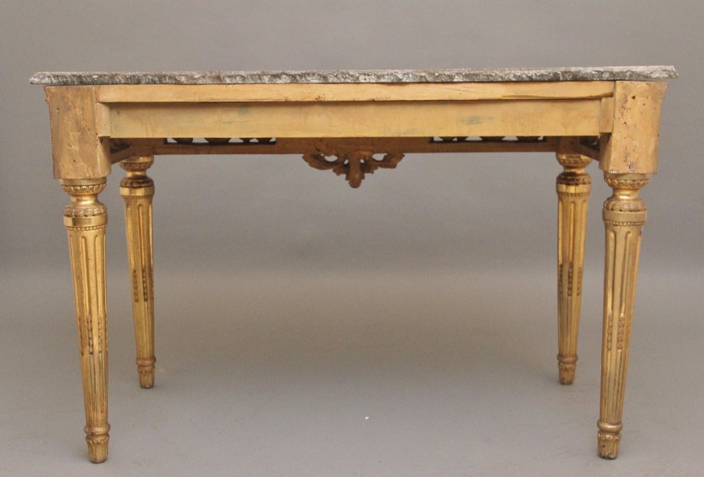 An 18th-century Italian Neoclassical console table featuring a grey marble top, pierced carved giltwood apron with central trophy carving, and fluted tapered legs. View VII