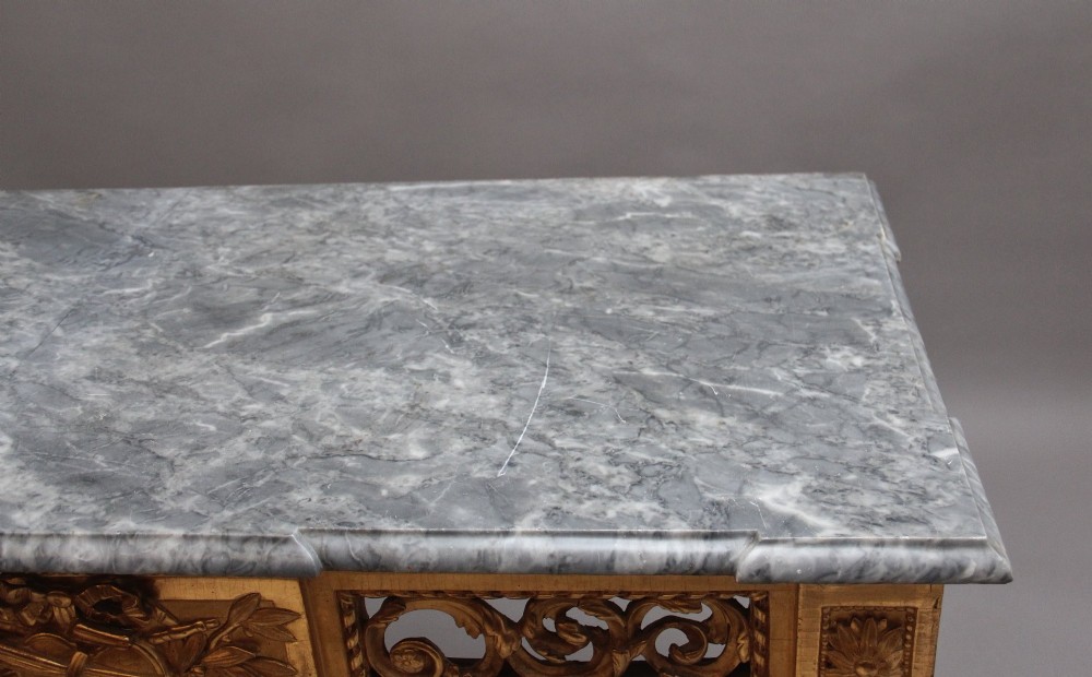 An 18th-century Italian Neoclassical console table featuring a grey marble top, pierced carved giltwood apron with central trophy carving, and fluted tapered legs. View VIII