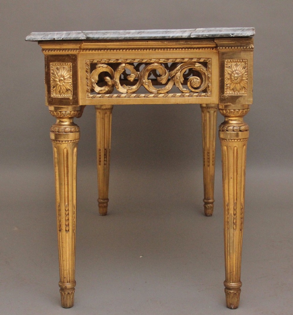An 18th-century Italian Neoclassical console table featuring a grey marble top, pierced carved giltwood apron with central trophy carving, and fluted tapered legs. View IX