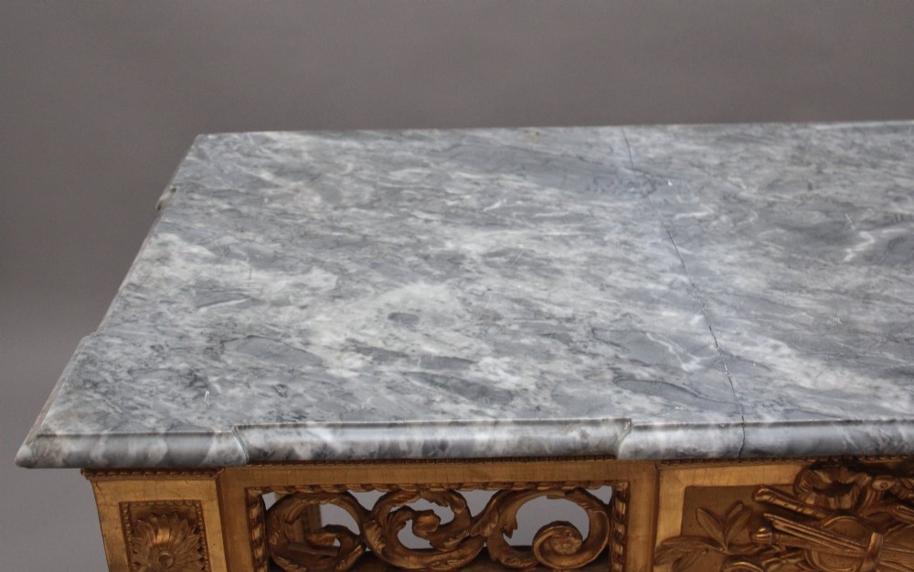 An 18th-century Italian Neoclassical console table featuring a grey marble top, pierced carved giltwood apron with central trophy carving, and fluted tapered legs. View XV