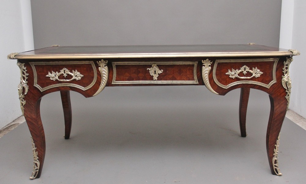 A 19th-century French kingwood writing desk with cabriole legs, ornate gilt-bronze ormolu mounts, three frieze drawers, and a dark inset leather writing top.