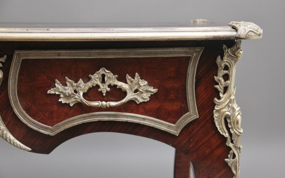 A 19th-century French kingwood writing desk with cabriole legs, ornate gilt-bronze ormolu mounts, three frieze drawers, and a dark inset leather writing top. View V