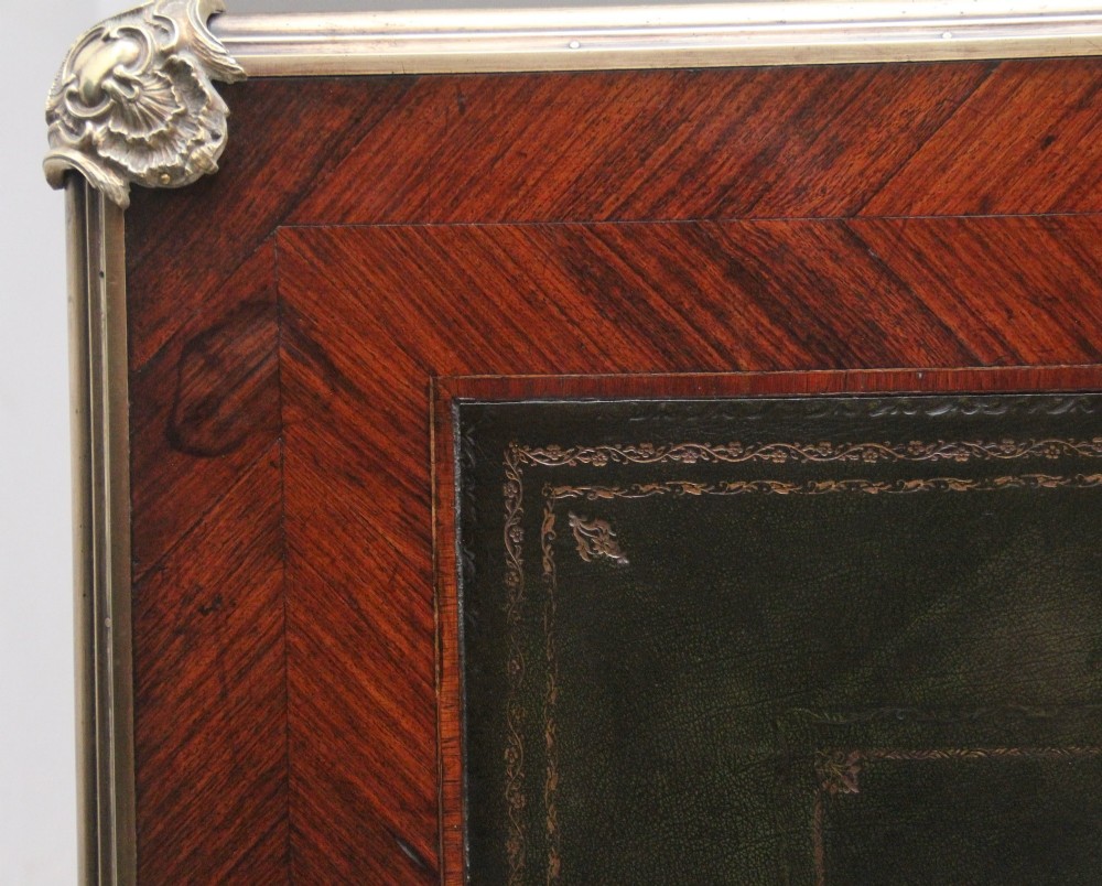 A 19th-century French kingwood writing desk with cabriole legs, ornate gilt-bronze ormolu mounts, three frieze drawers, and a dark inset leather writing top. View X