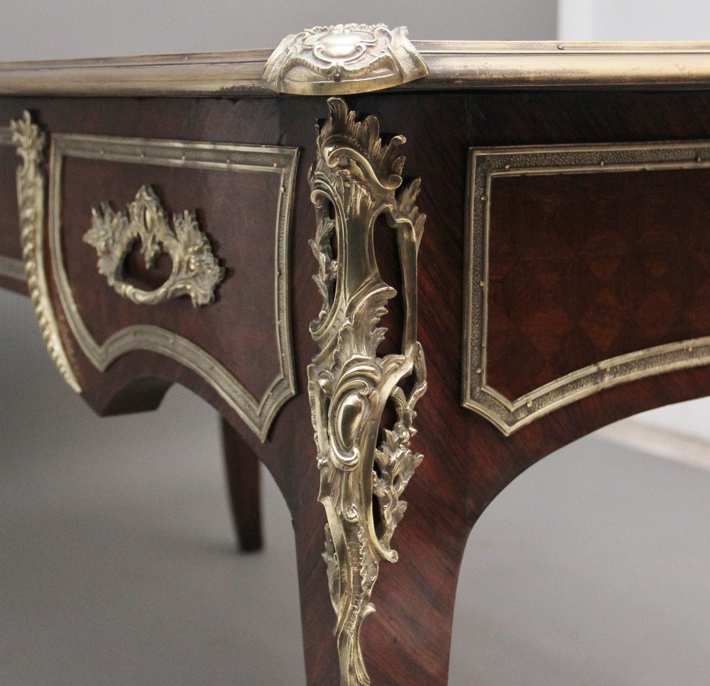 A 19th-century French kingwood writing desk with cabriole legs, ornate gilt-bronze ormolu mounts, three frieze drawers, and a dark inset leather writing top. View XII