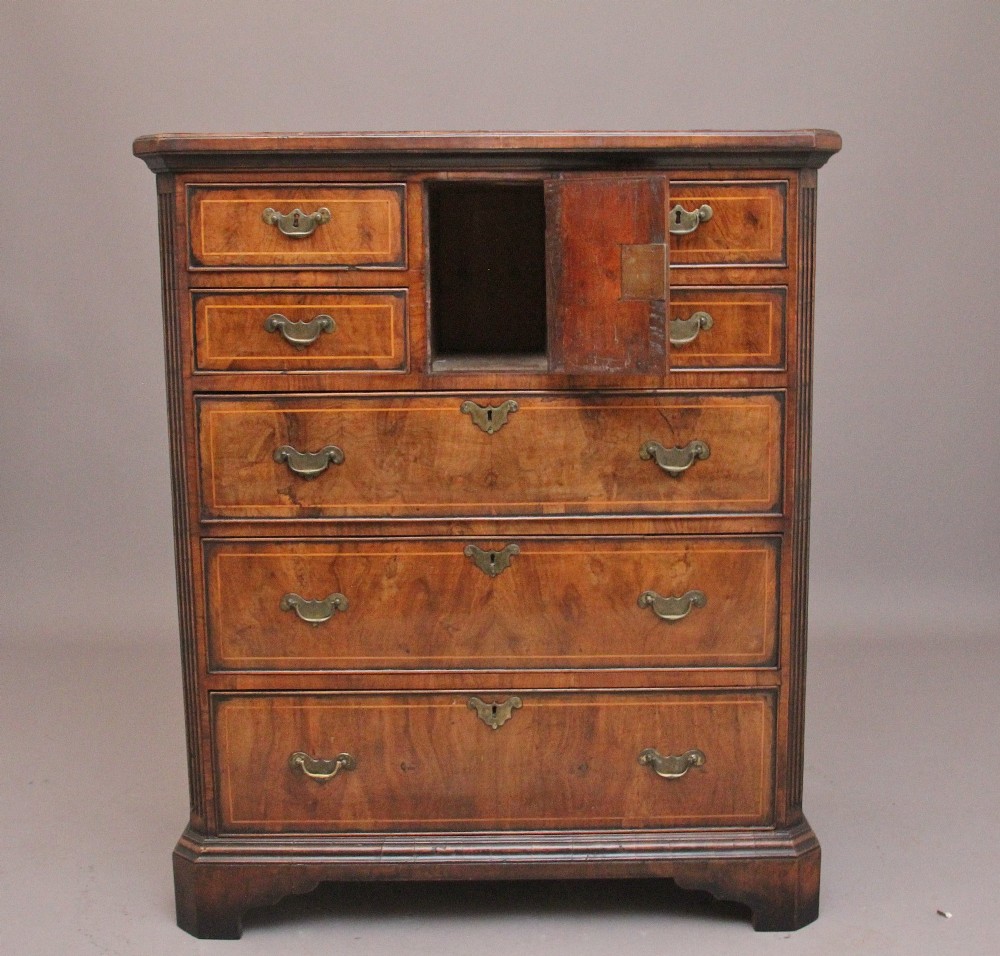 An early 18th-century George II walnut chest of drawers featuring crossbanded drawer fronts, brass handles, a central cupboard door, and bracket feet. View II