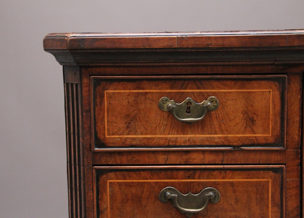An early 18th-century George II walnut chest of drawers featuring crossbanded drawer fronts, brass handles, a central cupboard door, and bracket feet. View IV