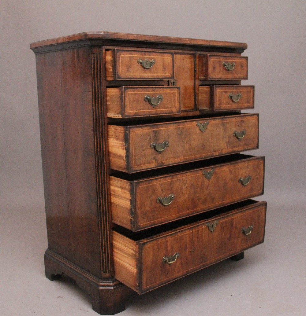 An early 18th-century George II walnut chest of drawers featuring crossbanded drawer fronts, brass handles, a central cupboard door, and bracket feet. View VII