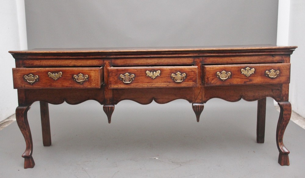 An early 18th-century oak dresser base featuring three brass-handled drawers, a scalloped apron with pendant drops, and cabriole legs. View II