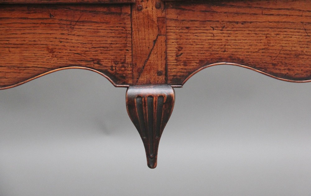 An early 18th-century oak dresser base featuring three brass-handled drawers, a scalloped apron with pendant drops, and cabriole legs. View V