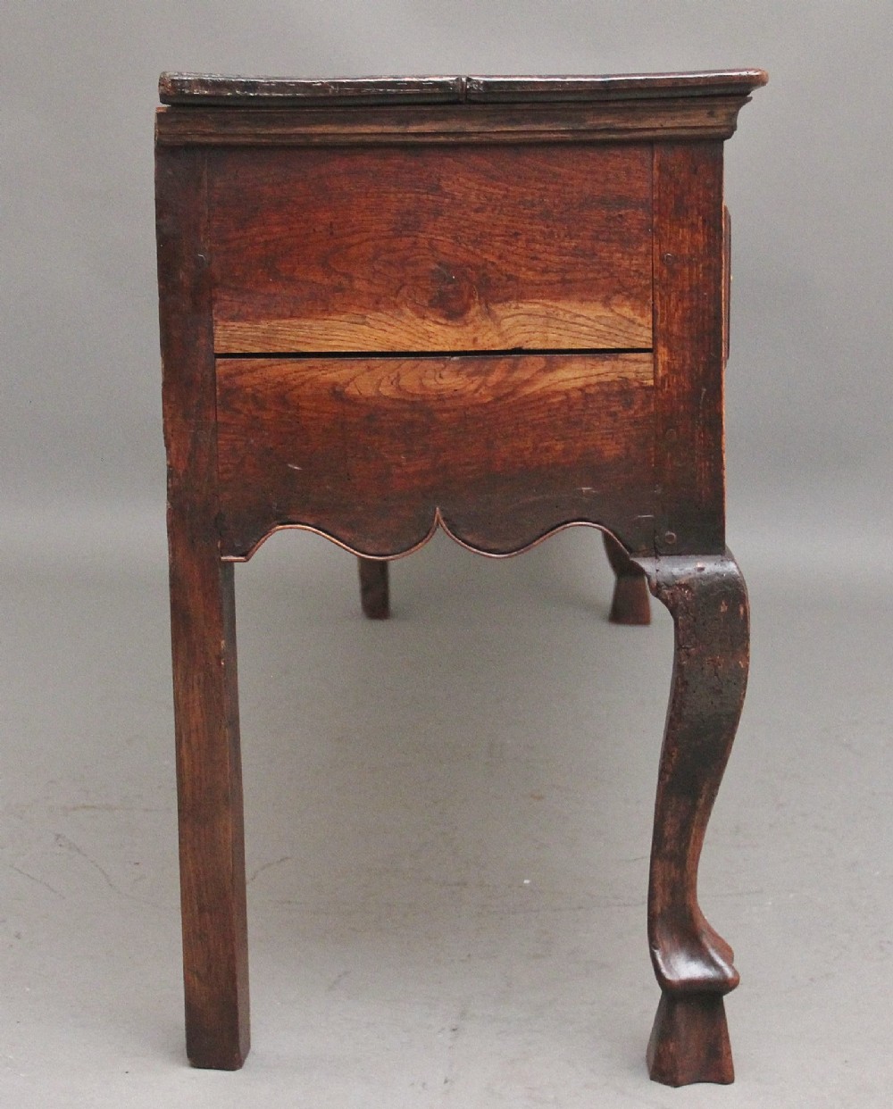 An early 18th-century oak dresser base featuring three brass-handled drawers, a scalloped apron with pendant drops, and cabriole legs. View VII