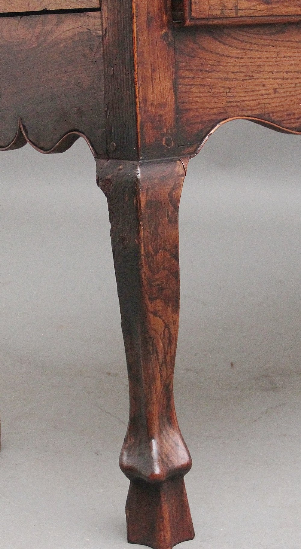An early 18th-century oak dresser base featuring three brass-handled drawers, a scalloped apron with pendant drops, and cabriole legs. View XI