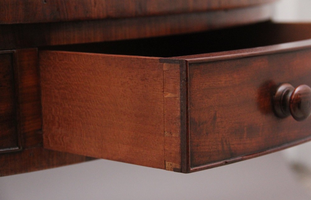 An early 19th century circular mahogany drum table featuring an inset green leather top, frieze drawers with knob handles, and a turned pedestal base. View VIII