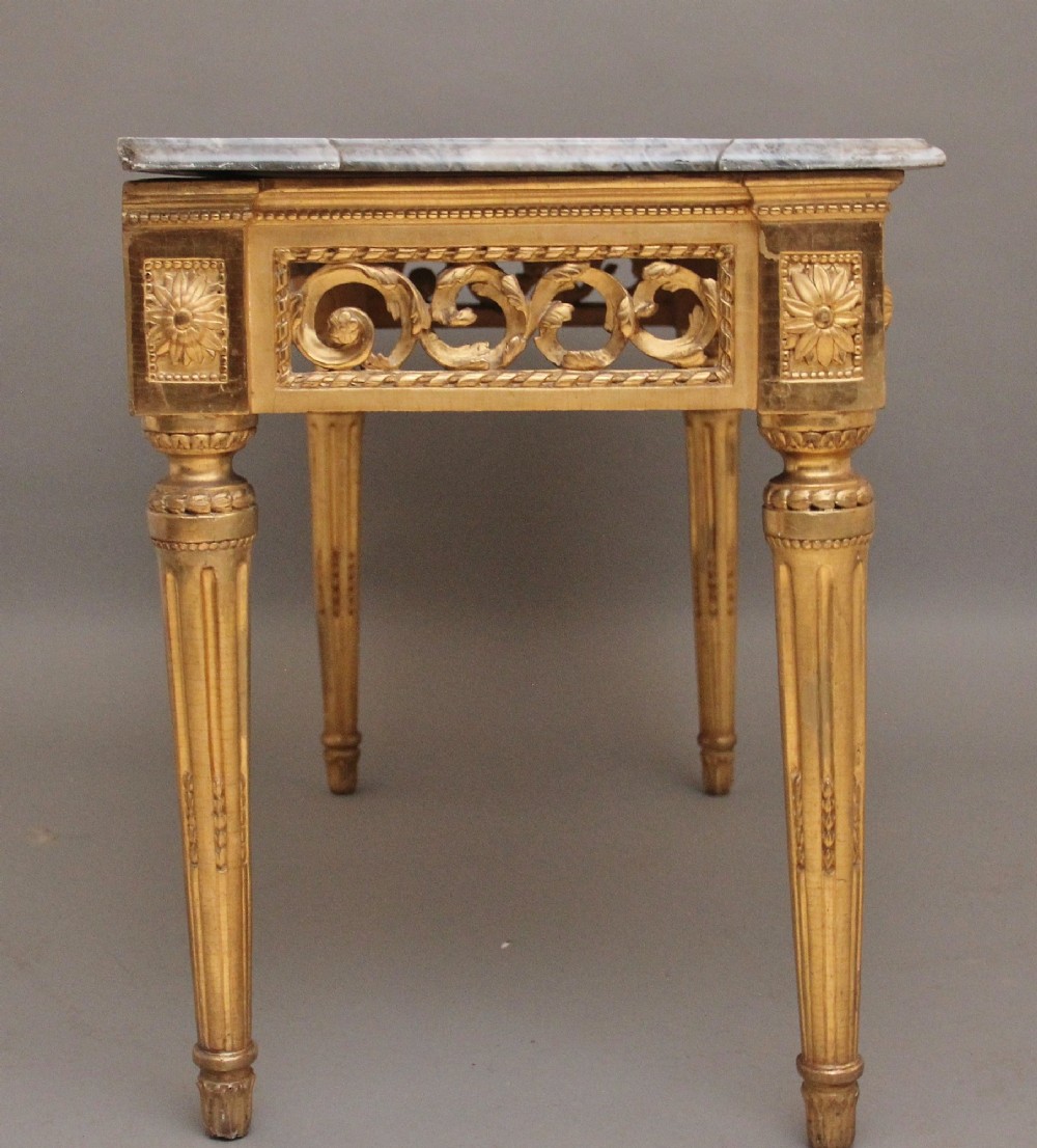 An 18th-century Italian giltwood console table featuring fluted tapered legs, an ornate carved central motif, and a grey marble top. View V